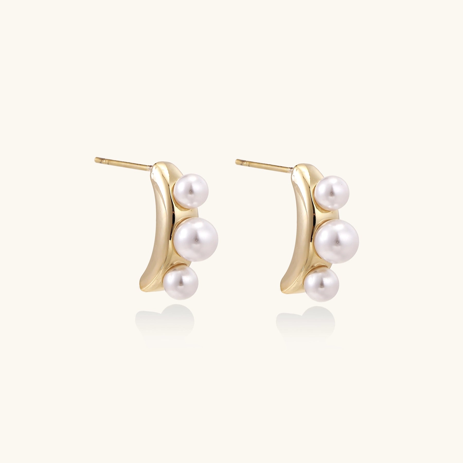 Delicate gold stud earrings with three lustrous white freshwater pearls arranged in an organic curved line.