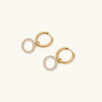 Gold-plated hoop earrings with circular cubic zirconia charm dangles displayed on neutral background.