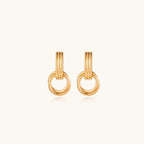 Geometric gold earrings with ribbed linear top section and circular drop elements on white background.