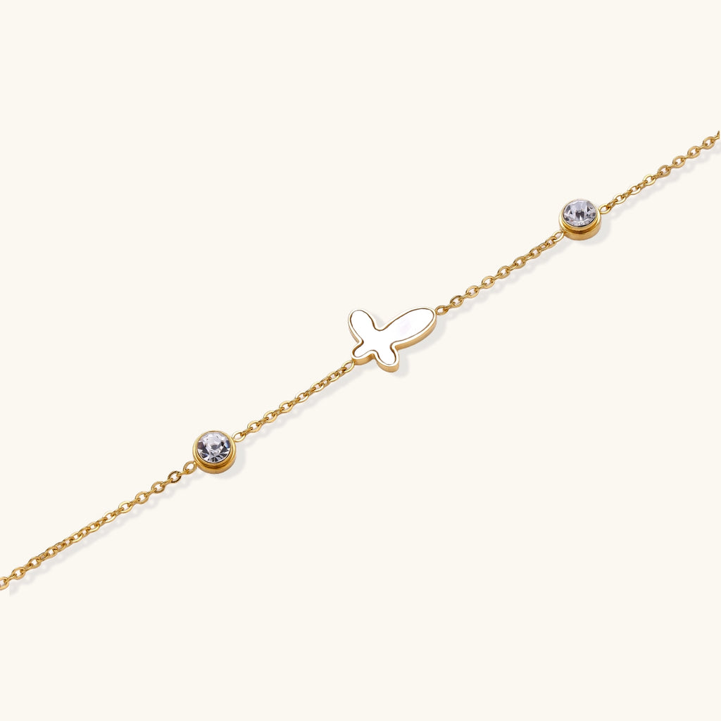 Delicate gold-plated bracelet featuring white mother-of-pearl cross charm and crystal accents on white background.