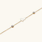 Delicate gold-plated bracelet featuring white mother-of-pearl cross charm and crystal accents on white background.